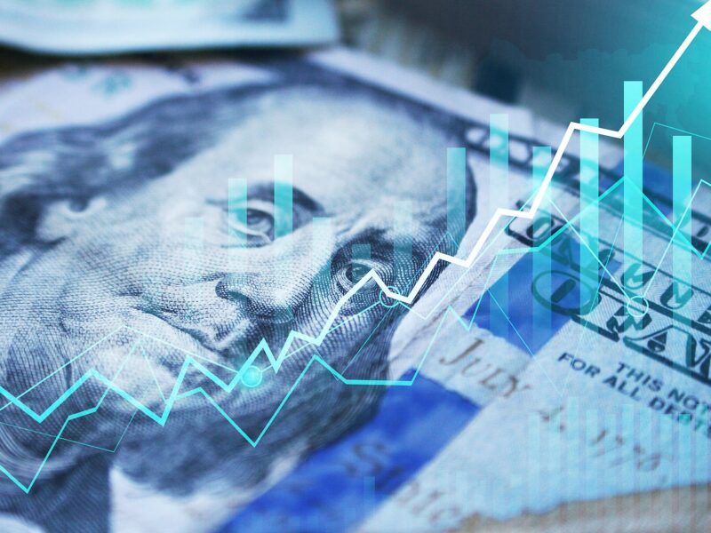 Close-up of a US hundred-dollar bill with turquoise stock charts and an upward trend overlay.