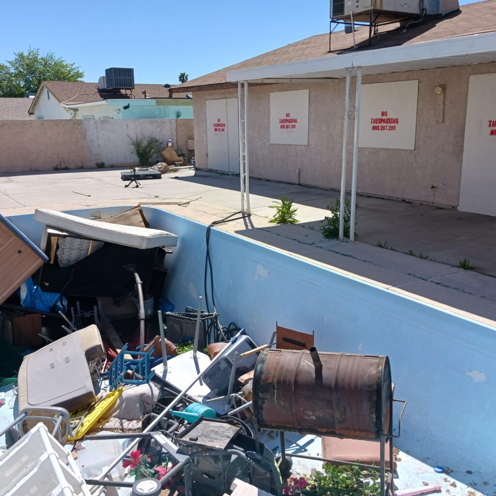 Cluttered backyard with a blue boat and scattered debris against a wall with No Trespassing signs in red letters.