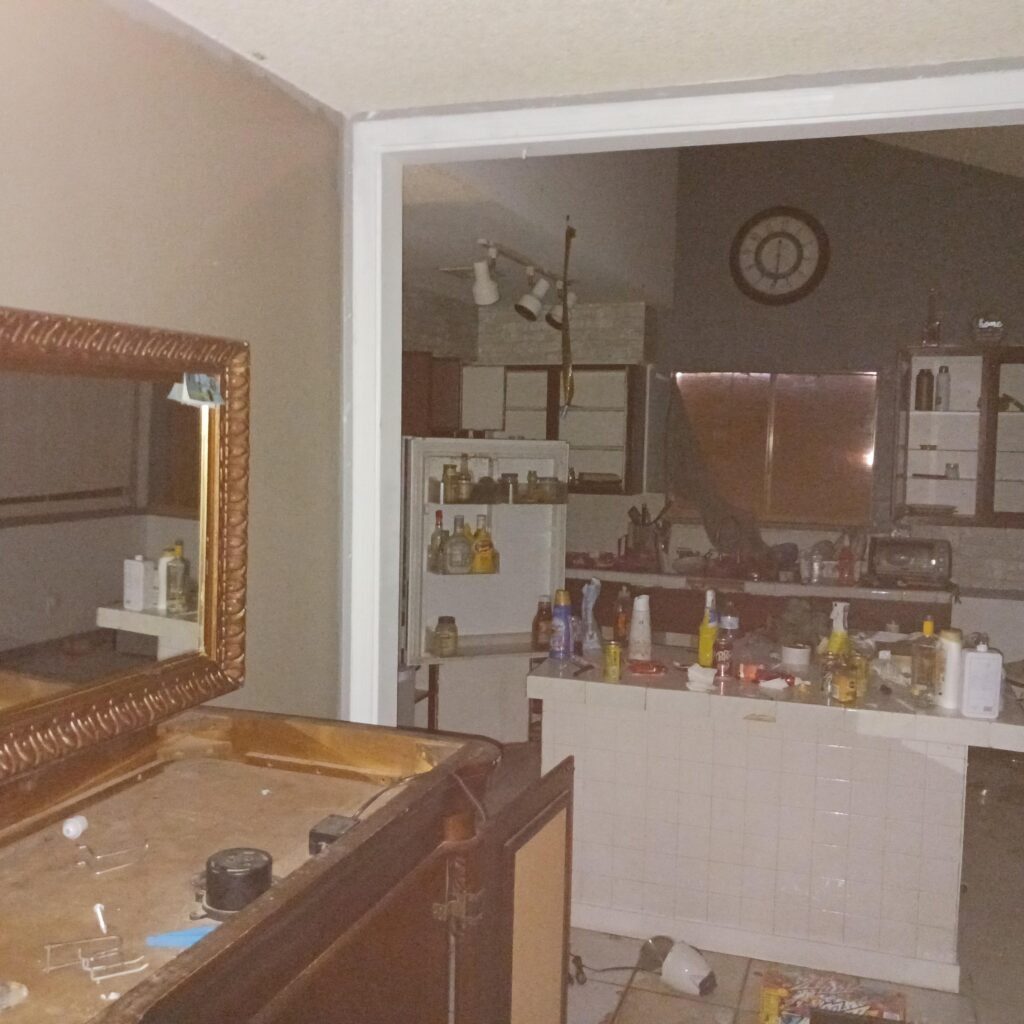 Dimly lit kitchen with an open refrigerator showing bottles and shelves, and a round clock on the wall behind.