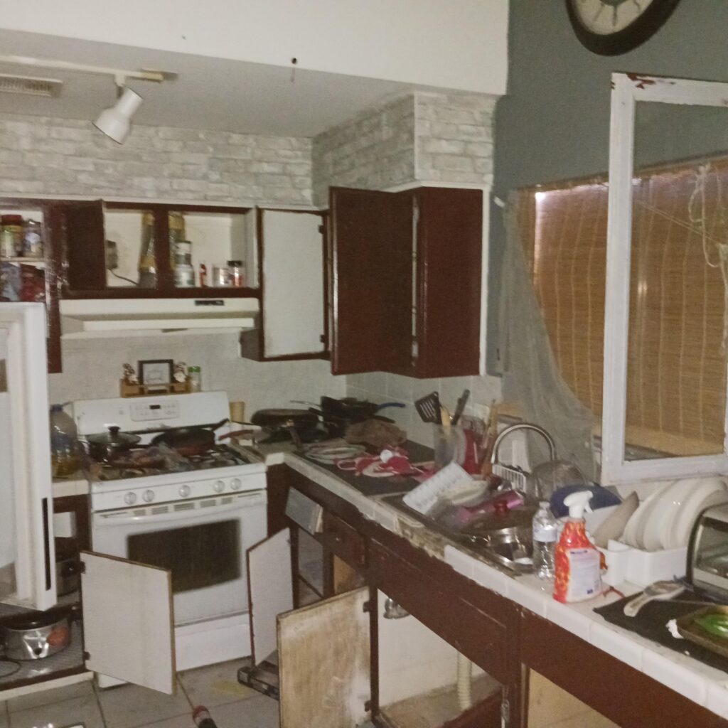Cluttered kitchen with open cabinets, a white stove, and many items scattered on the counter and floor as if mid-cleanup.
