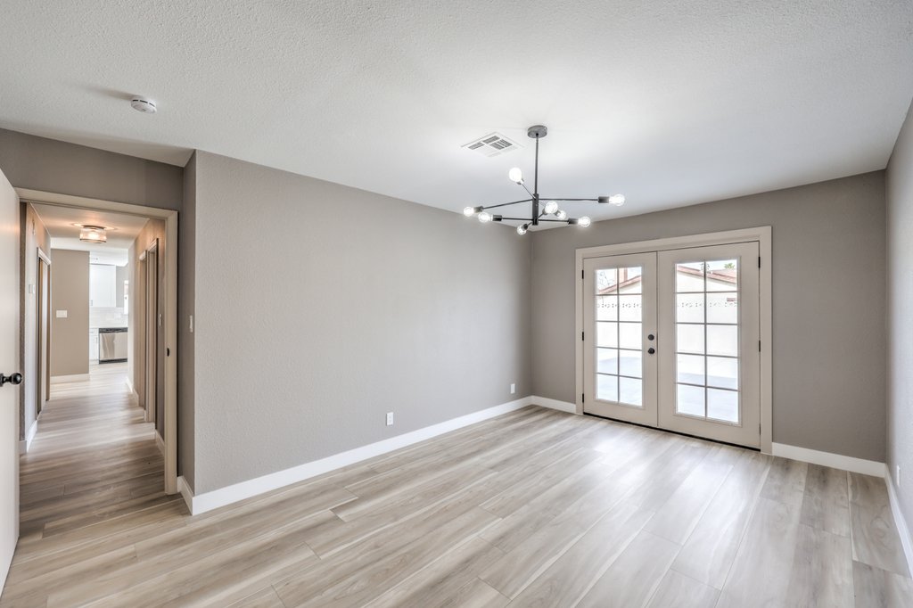 Living room with gray walls, light wood flooring, and French doors to the outdoors beneath a modern chandelier.