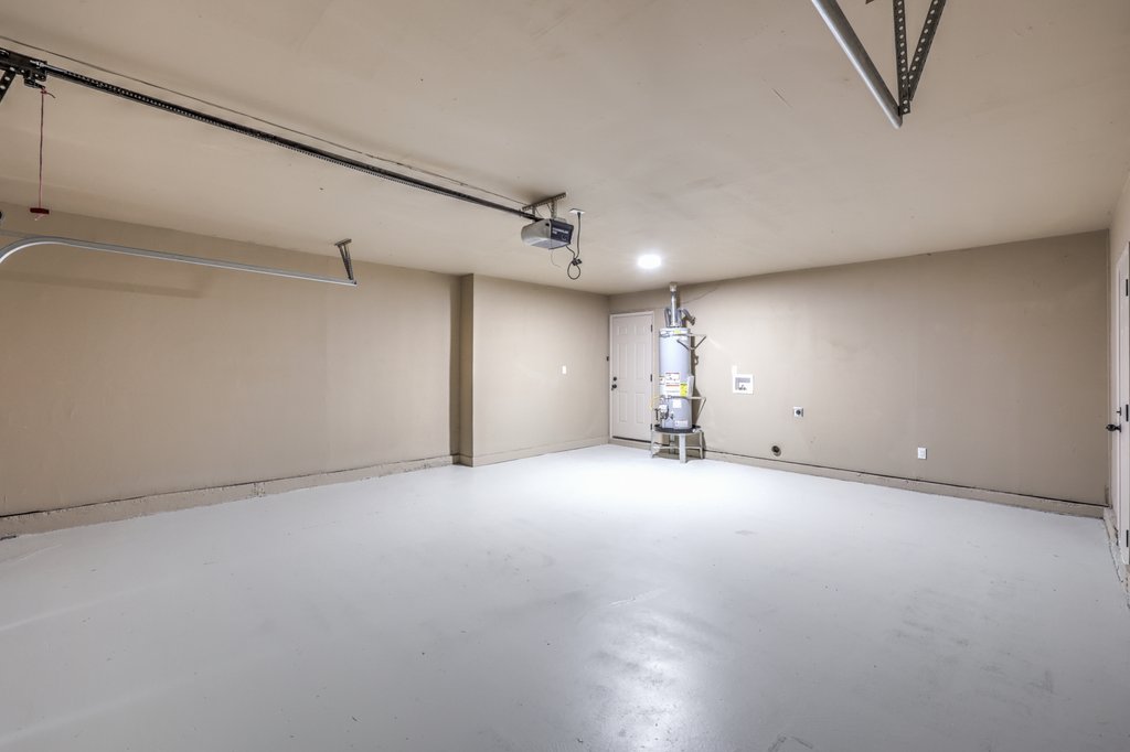 Empty residential garage with beige walls, concrete floor, and a water heater near the back wall.