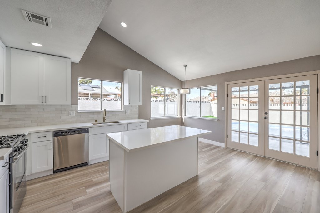 Bright white kitchen with an island, white cabinets, stainless steel appliances, and French doors to the outdoors.