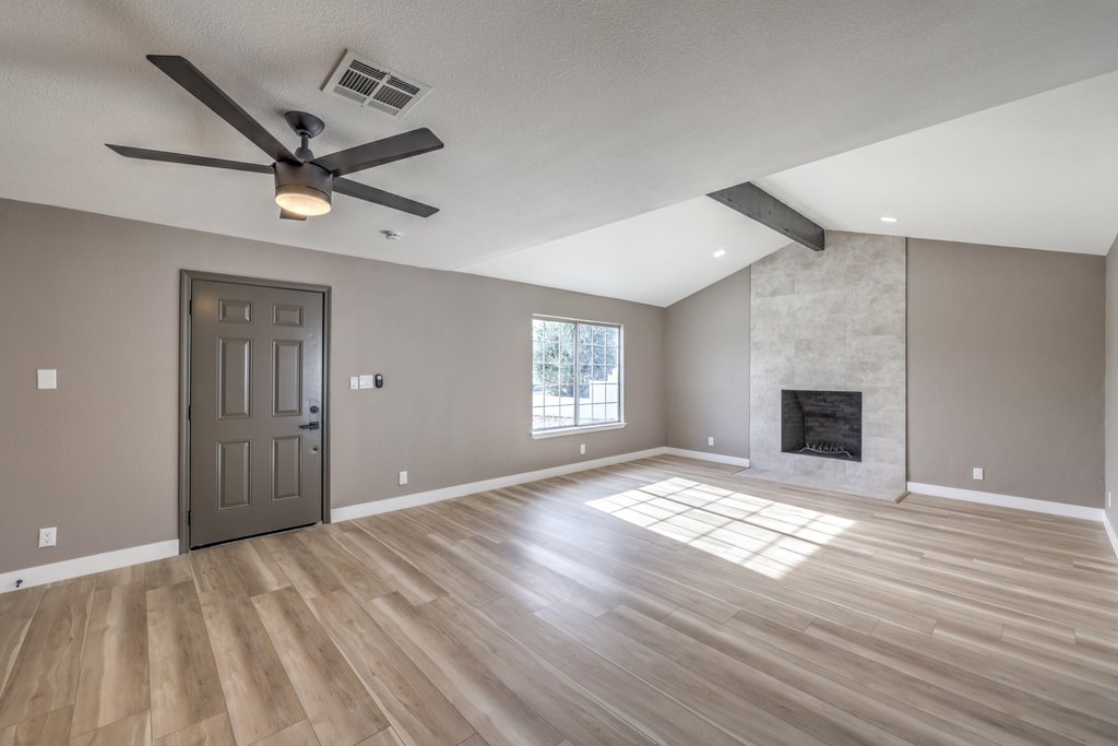 Spacious living room with light wood floors, gray walls, a ceiling fan, and a modern fireplace.