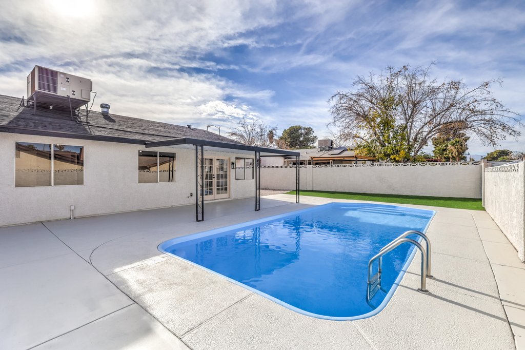 Backyard with a rectangular blue pool, white concrete deck, and a single-story house with a covered patio.